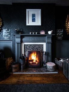 Cozy living room with a lit fireplace, dark walls, and framed art above a mantel.