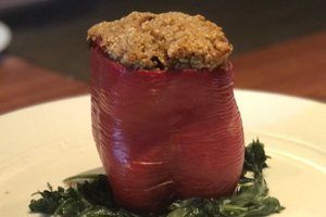 A stuffed pepper is on a white plate with greens.