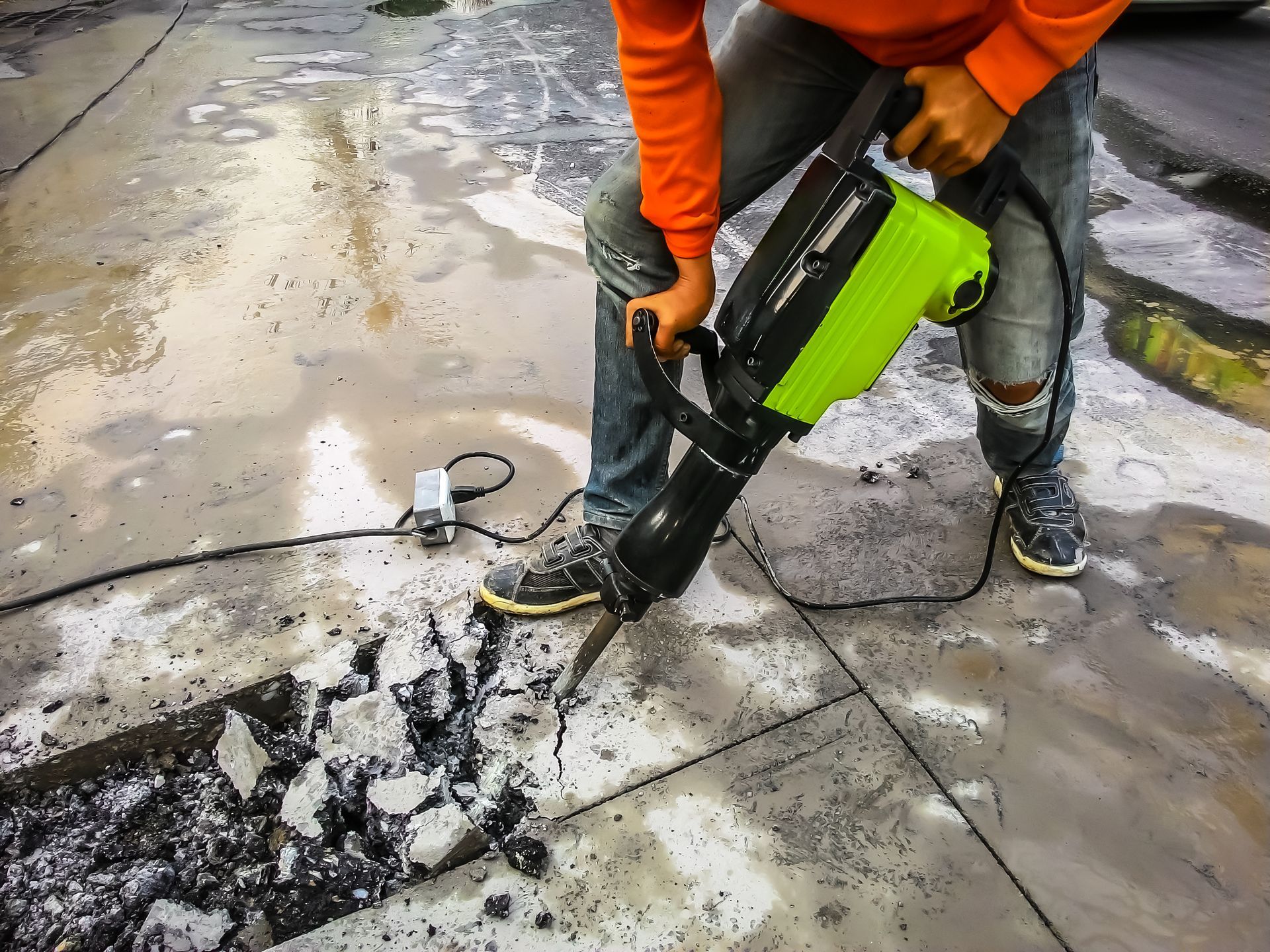 A man is using a hammer to break concrete on a sidewalk.
