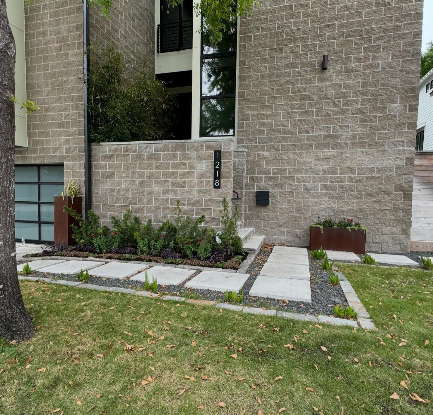 Modern house with a stone facade, concrete walkway, and landscaped front yard.