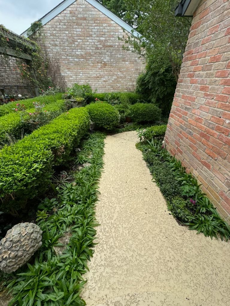 A stone path winds through a garden with green hedges and brick walls.