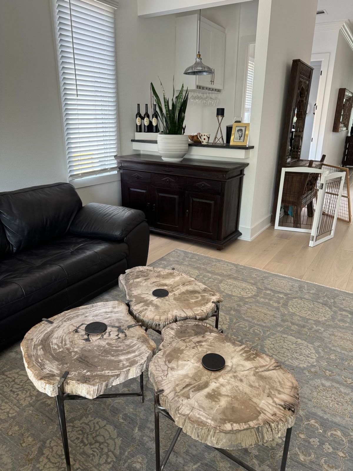 Three wood slab tables with black metal legs, set on a patterned rug in front of a dark cabinet and sofa.