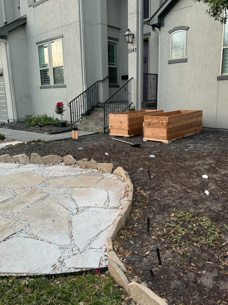 Exterior view of a house with two wooden planters on the dirt landscape. A stone walkway is in the foreground.