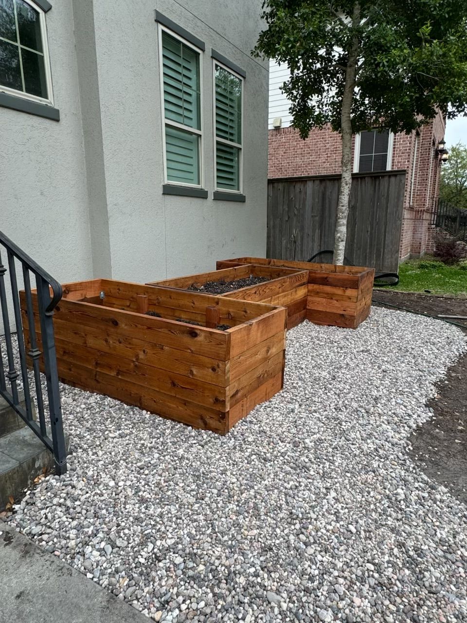 Wooden raised garden beds on gravel next to a building with windows and stairs.