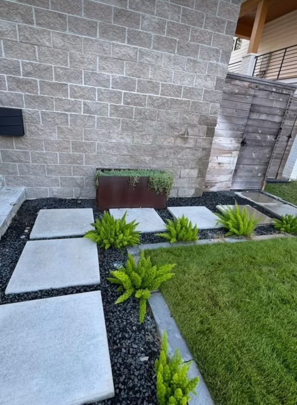 Concrete pavers and greenery lead to a modern building with a dark brick facade and a rusted metal planter box.