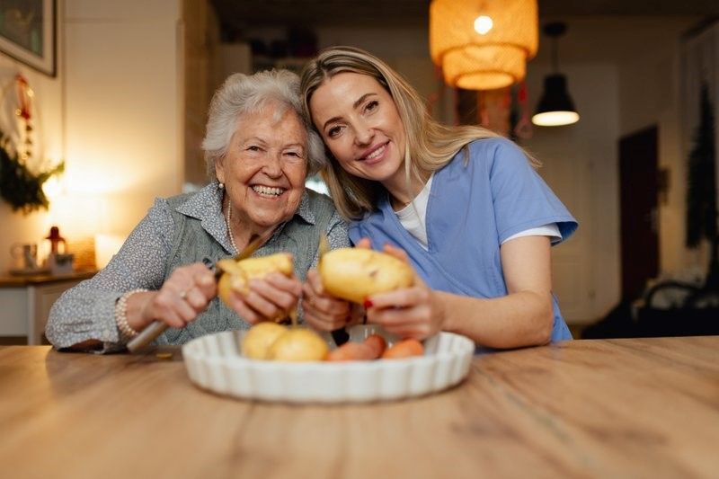 An elderly woman and a nurse are sitting at a table eating fruit.