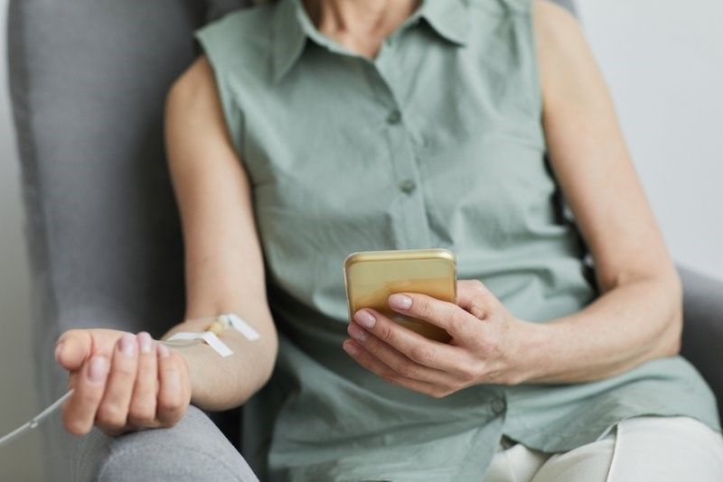 Woman receiving IV therapy while browsing on her phone. Woman receiving IV therapy while browsing on her phone.