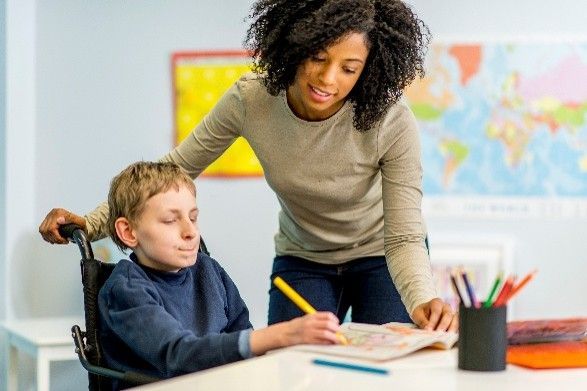 Teacher helping student write at a desk in a classroom