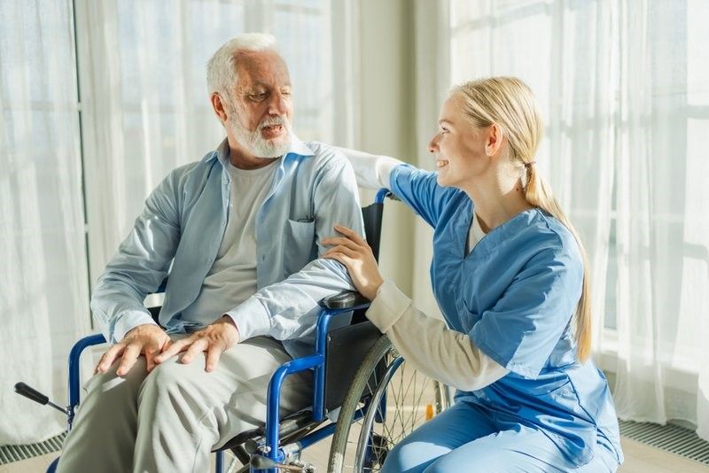 A nurse is talking to an elderly man in a wheelchair.
