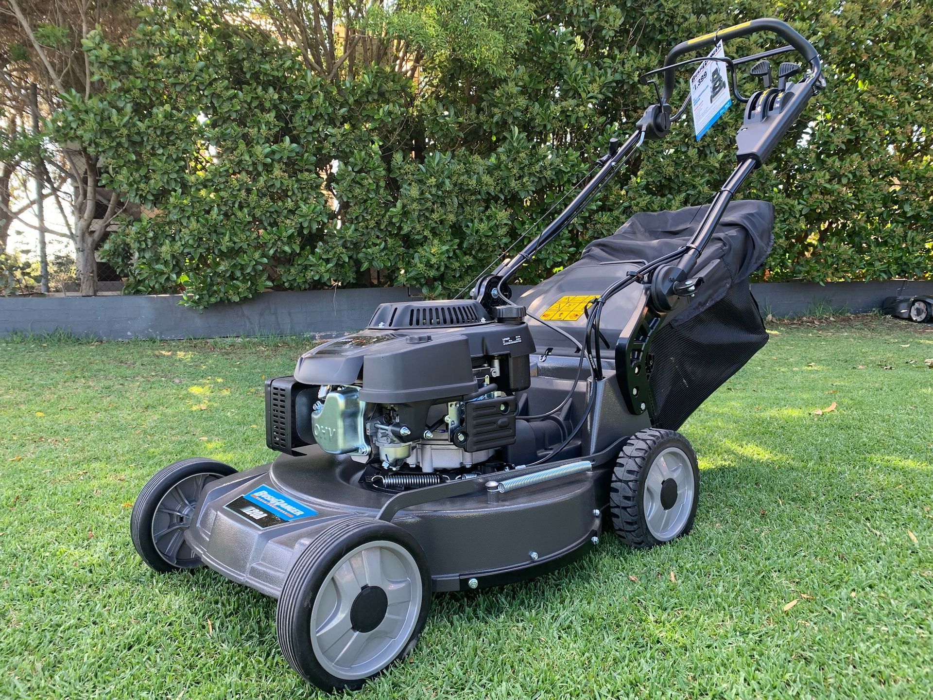 Dark gray lawnmower on grass with a black collection bag, trees in the background — M.M & Mechanical in Dubbo, NSW