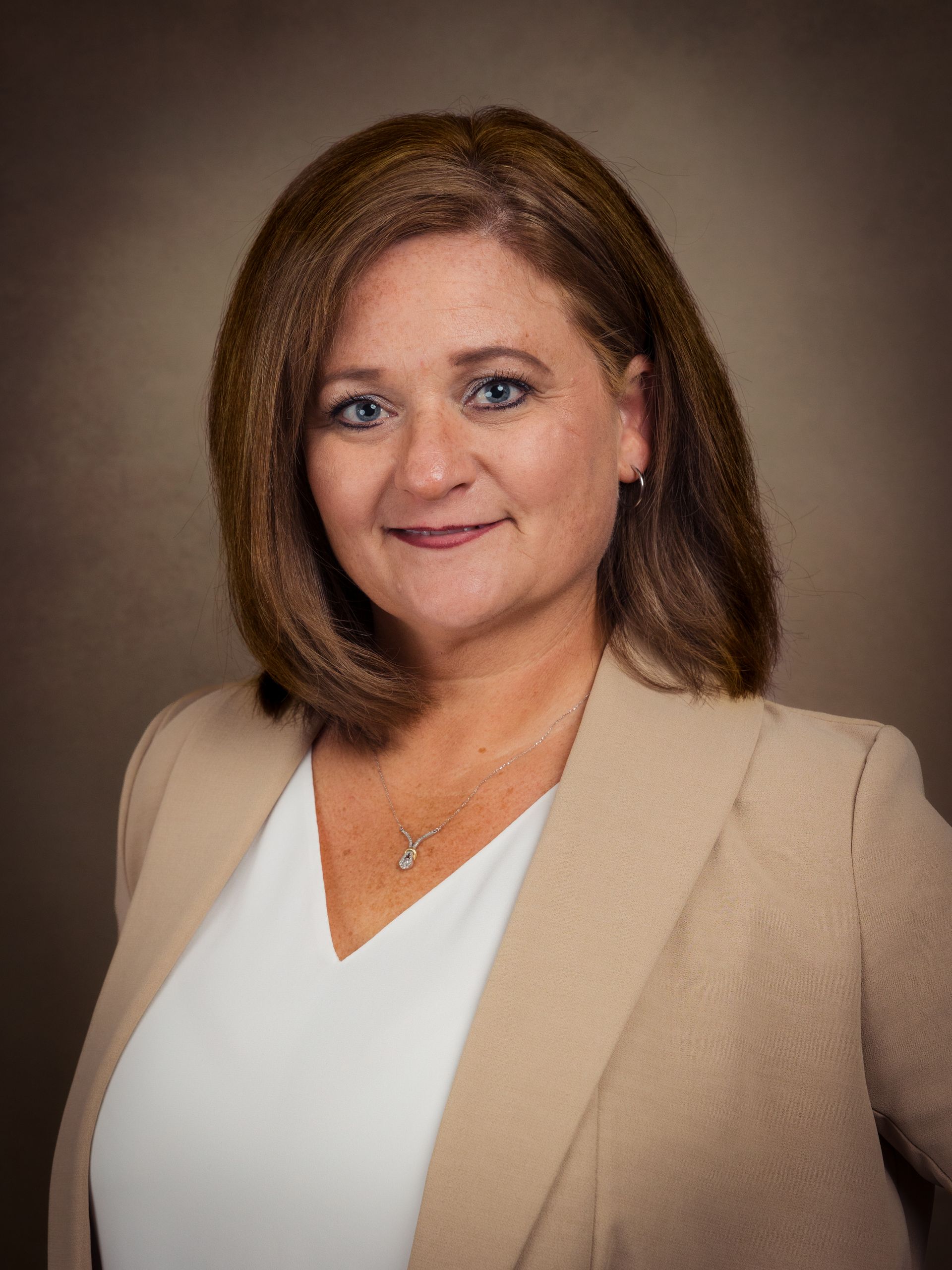 Portrait of a woman in a beige blazer and white top against a brown studio backdrop