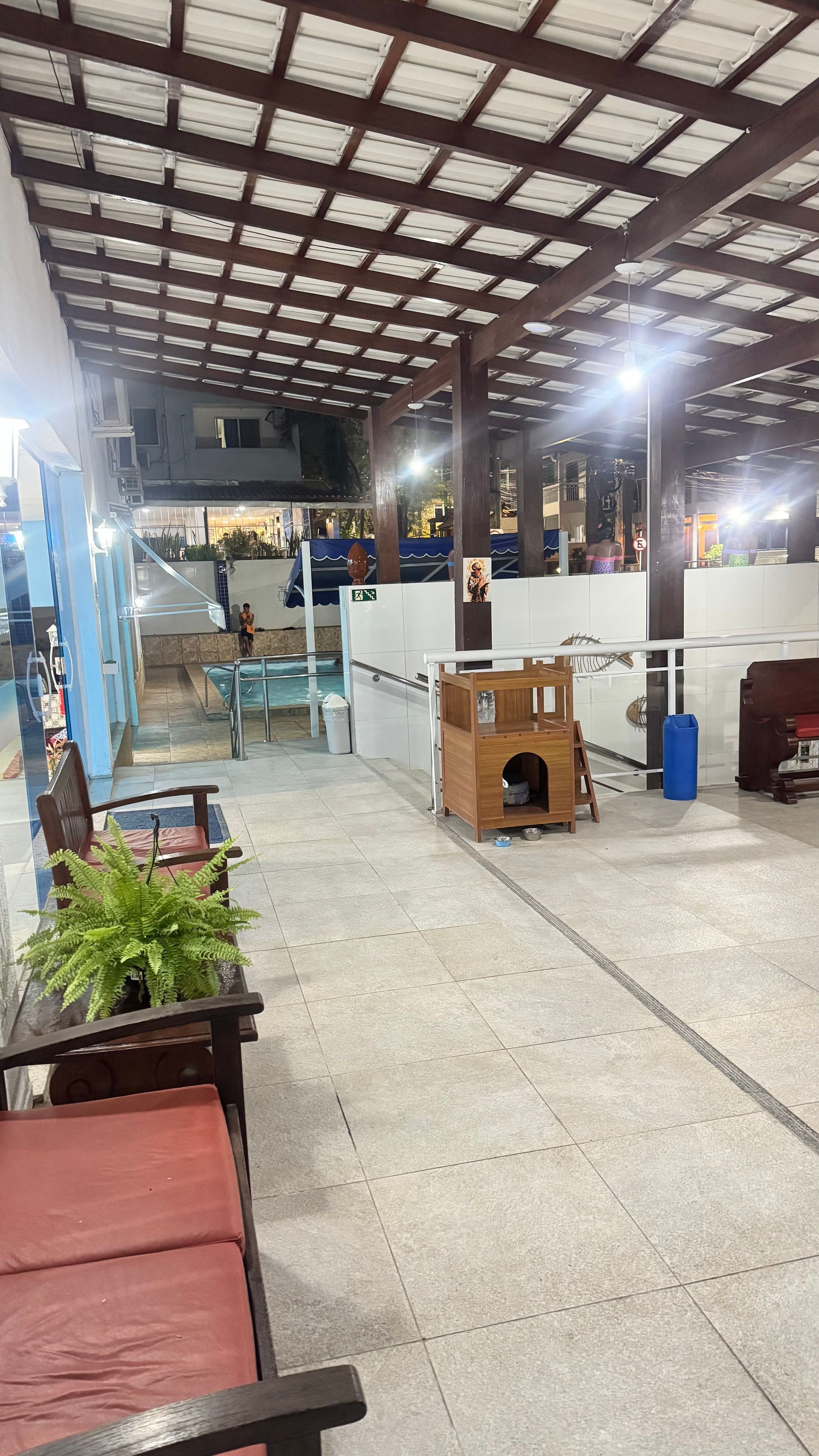 Galpão industrial interno com teto metálico alto, iluminação intensa e equipamentos sobre piso de concreto.