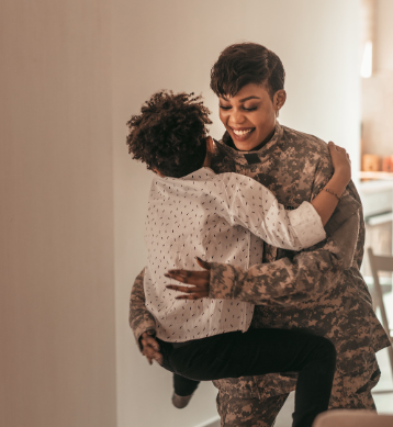 A woman in a military uniform is holding a child in her arms.