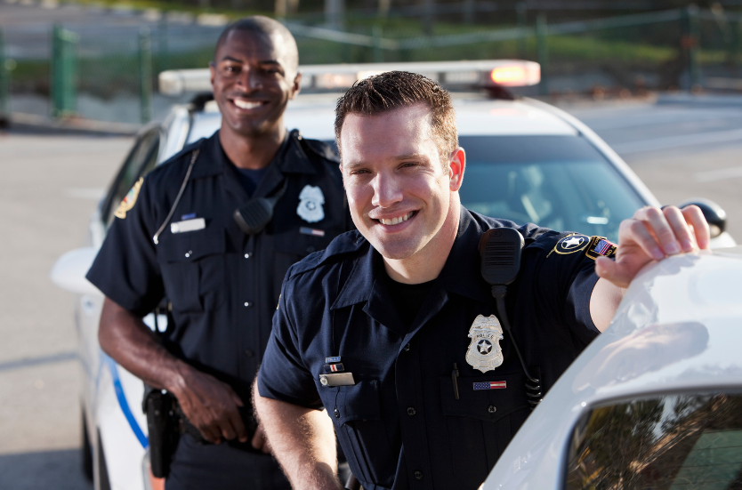 Two police officers are posing for a picture in front of a police car.