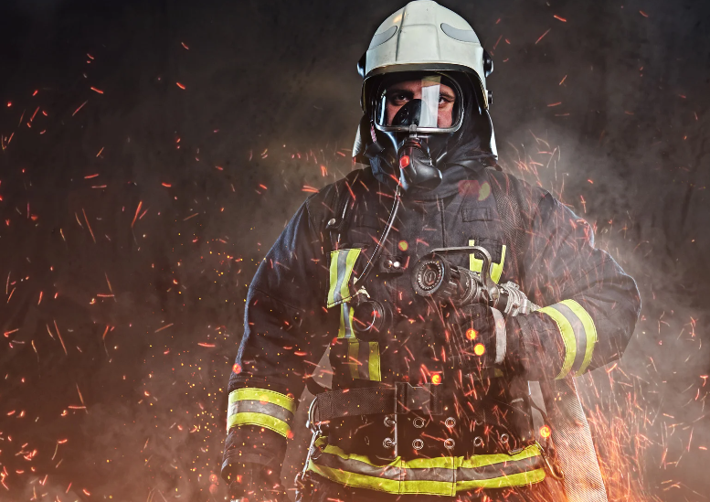 A fireman wearing a helmet and gas mask is standing in front of a fire.