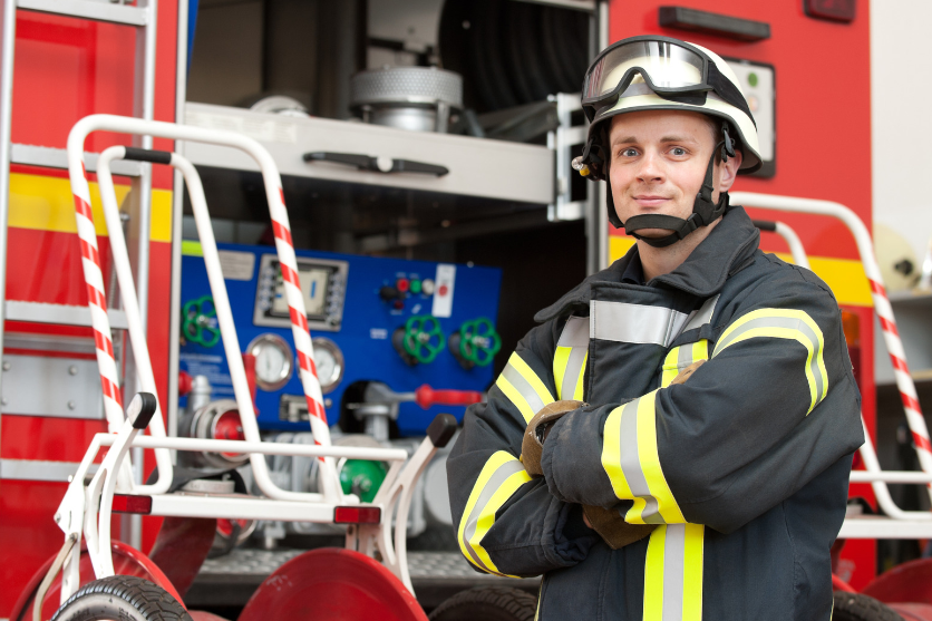 A fireman is standing in front of a fire truck with his arms crossed.