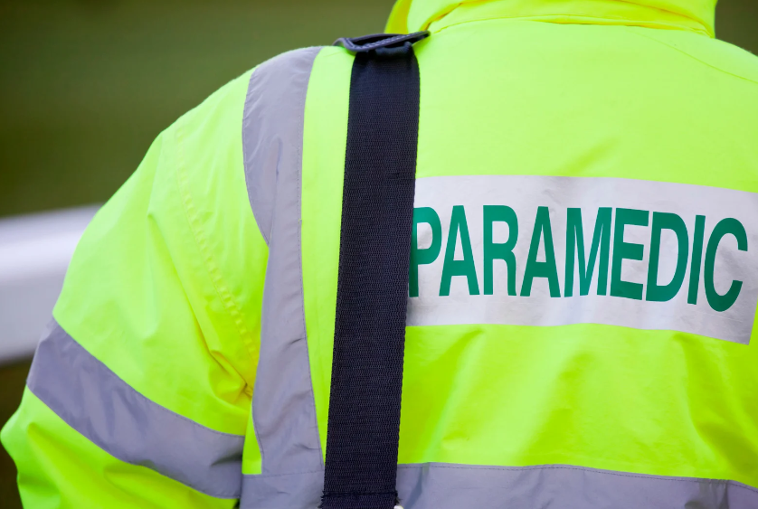 A paramedic is wearing a yellow jacket with the word paramedic on the back.