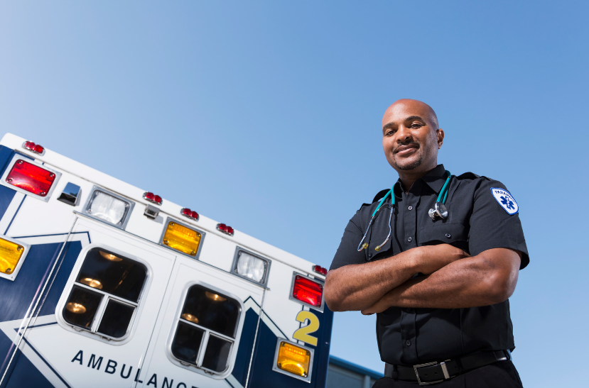 A man is standing in front of an ambulance with his arms crossed.