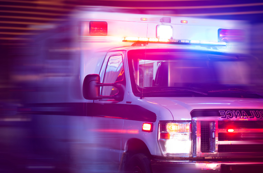 An ambulance is driving down the street at night with its lights on.
