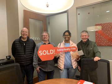 a group of people standing around a table holding a sold sign .