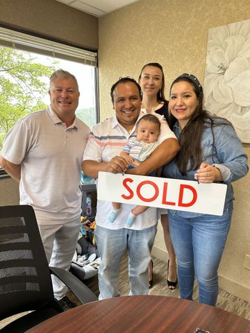a group of people standing around a table holding a sold sign .