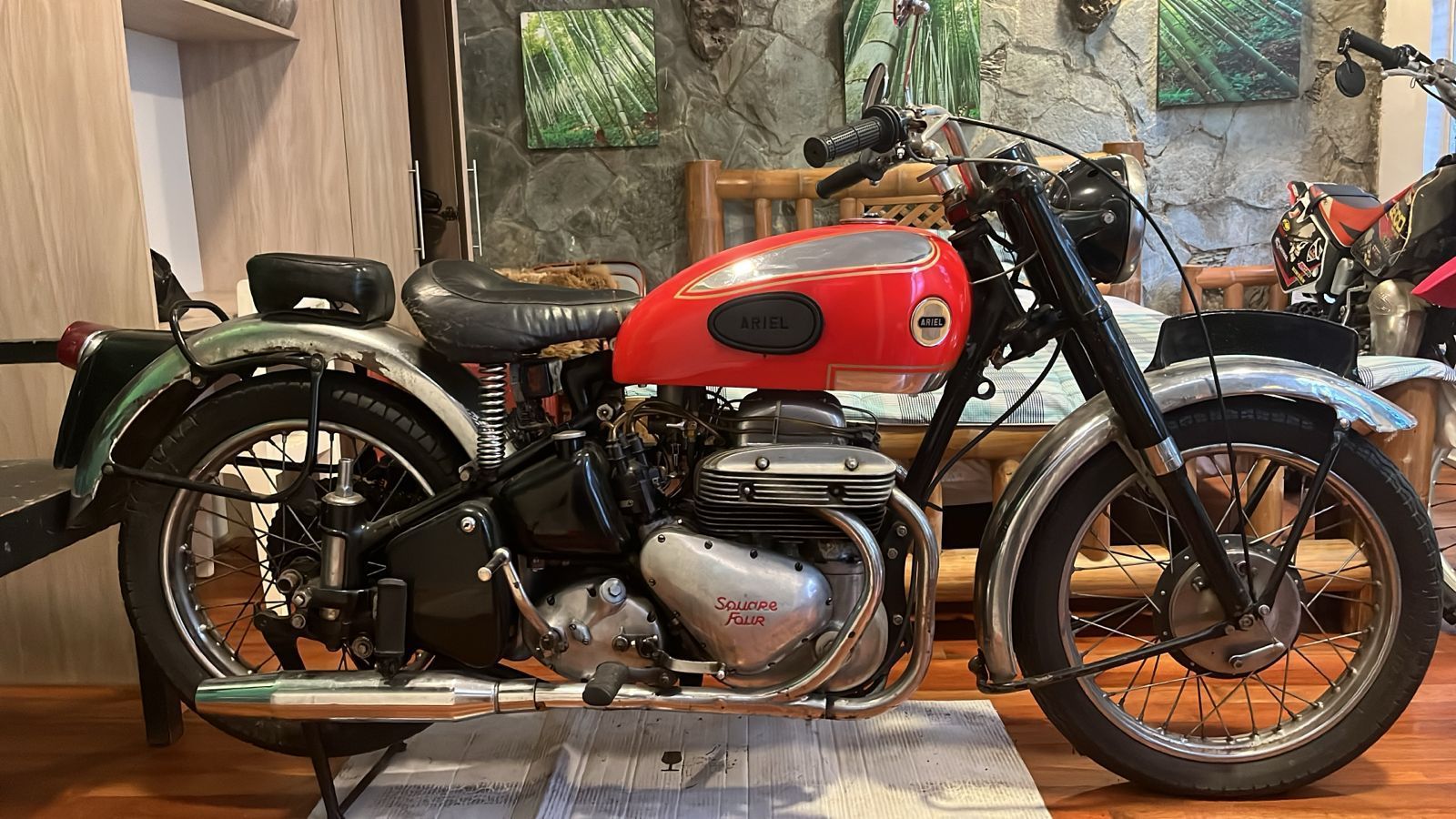 Motocicleta vintage roja y negra, estacionada en un lugar cerrado. Motor plateado, llantas de radios y guardabarros negros.