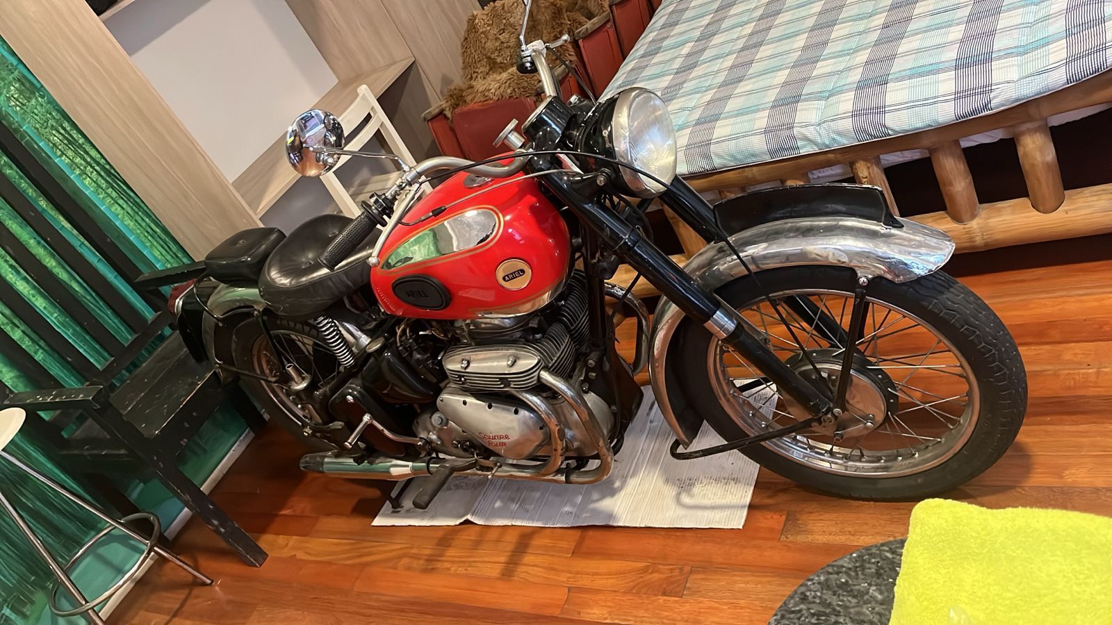 Motocicleta vintage roja y negra estacionada en el interior sobre un piso de madera.
