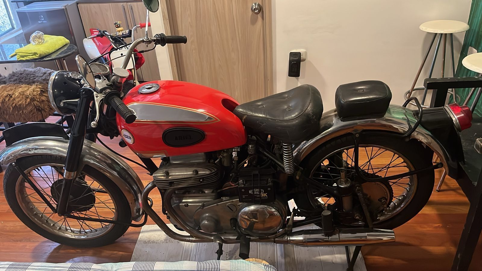 Motocicleta vintage roja y plateada estacionada en interior, asiento y guardabarros negros, detalles cromados.
