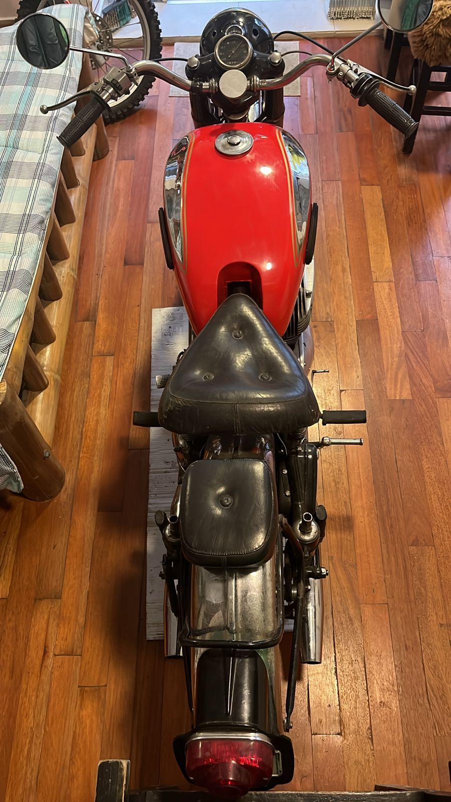Vista de arriba hacia abajo de una motocicleta vintage roja y negra sobre un piso de madera.