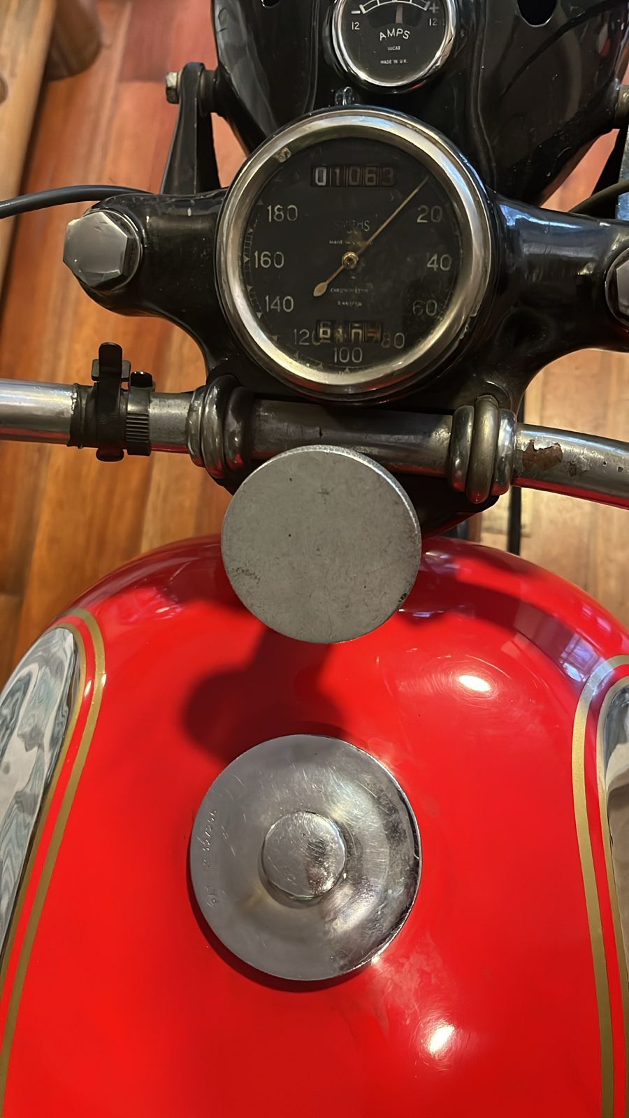 Tanque de combustible de motocicleta vintage de color rojo con tapa plateada y medidores en el manillar.