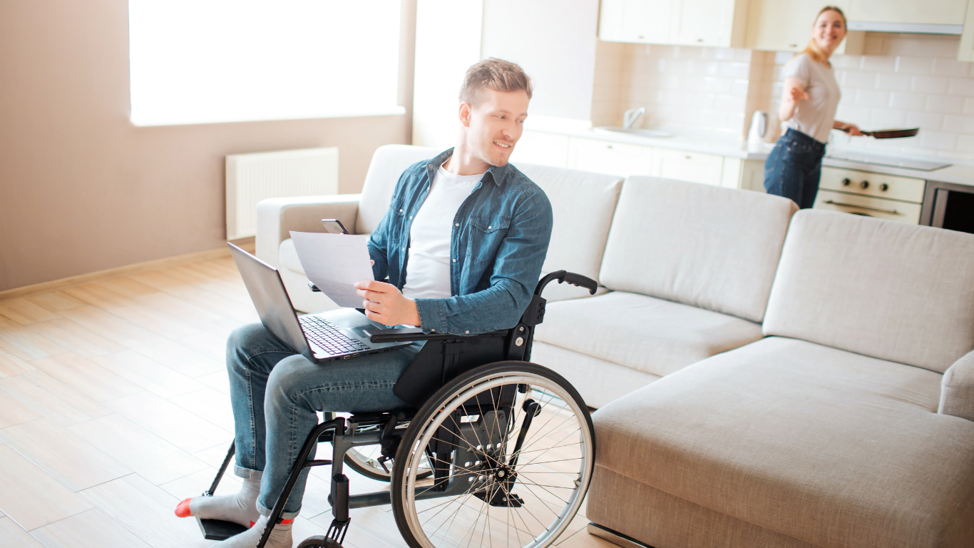 A man in a wheelchair is sitting on a couch using a laptop computer.
