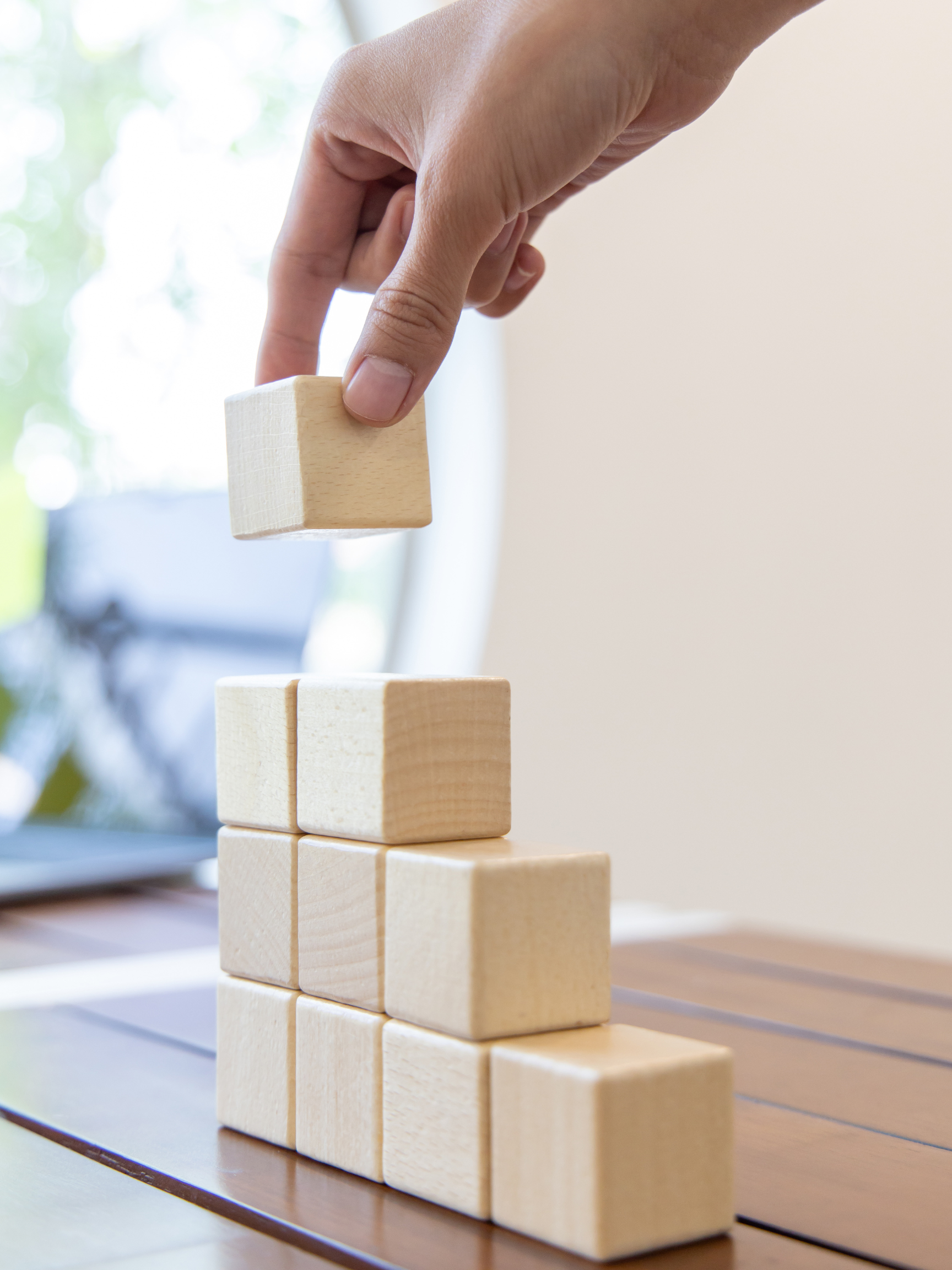 A person is stacking wooden blocks on top of each other on a wooden table.