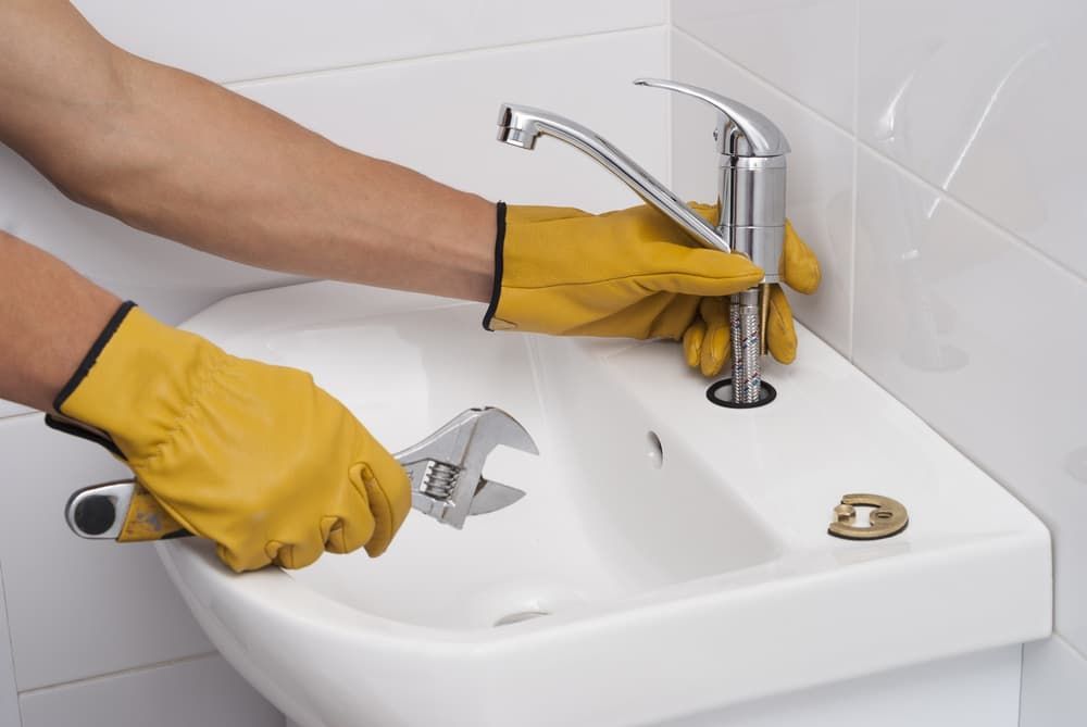 A Person Wearing Yellow Gloves is Fixing a Sink With a Wrench — Mainline Plumbing & Civil Pty Ltd In Wellington, NSW