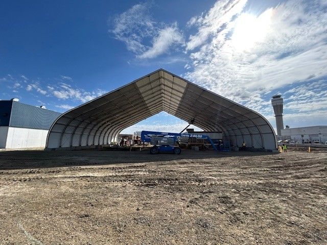 Large tent-like construction shelter over a dirt worksite with a crane in the center.