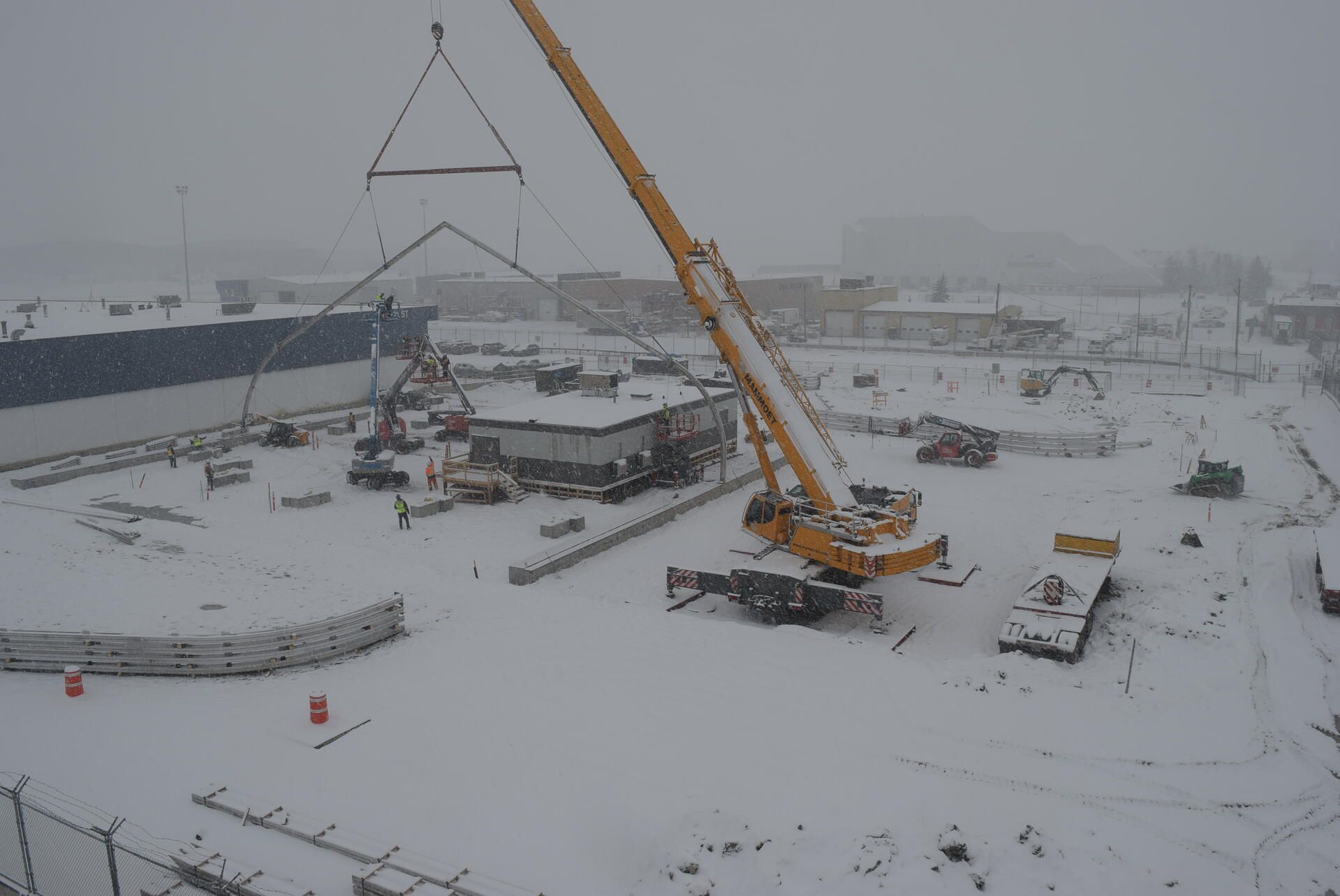 Snowy construction site with a crane lifting a steel frame in the background