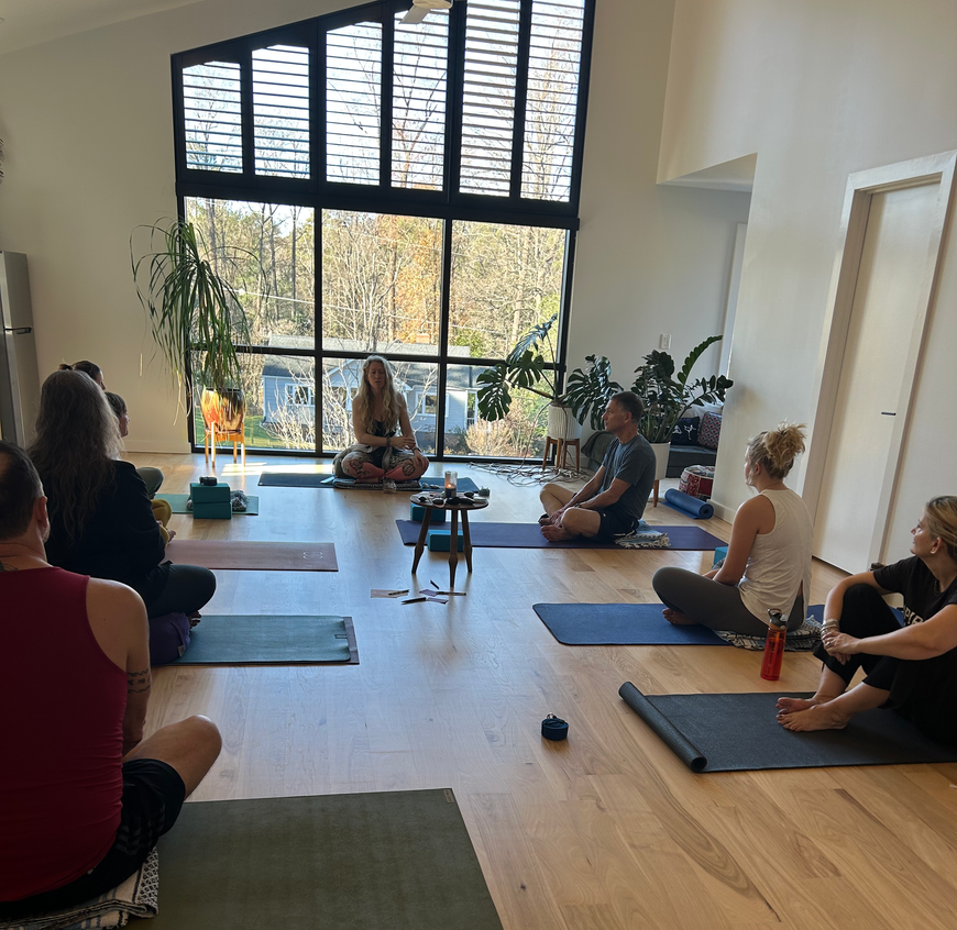 A group of people are sitting on yoga mats in a room at Healing House NC