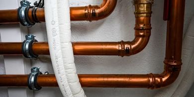 Copper plumbing pipes with metal clamps and a white insulated pipe in a wall cavity