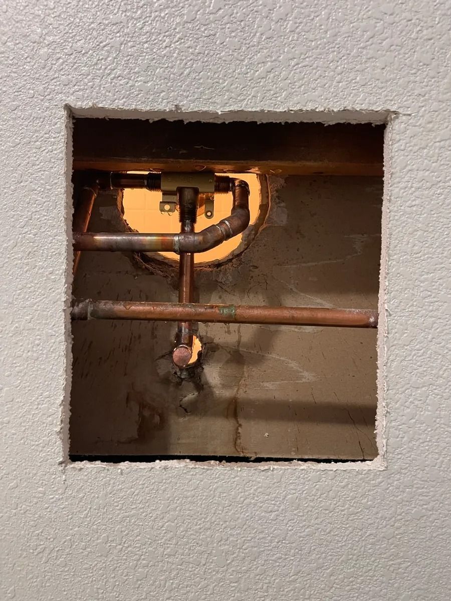 Wall cutout showing exposed copper pipes and a valve inside a building wall.