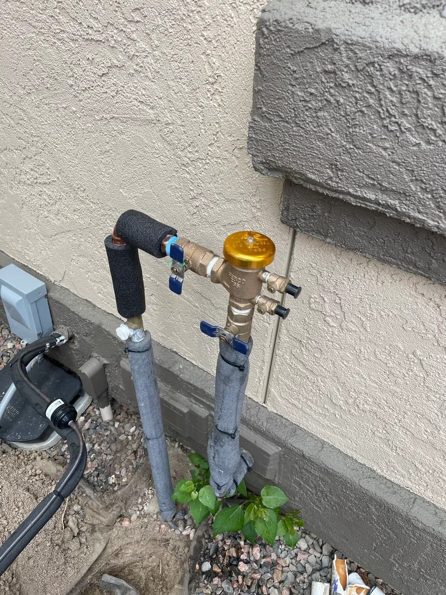 Outdoor utility pipes with a yellow-capped valve beside a wall and concrete step