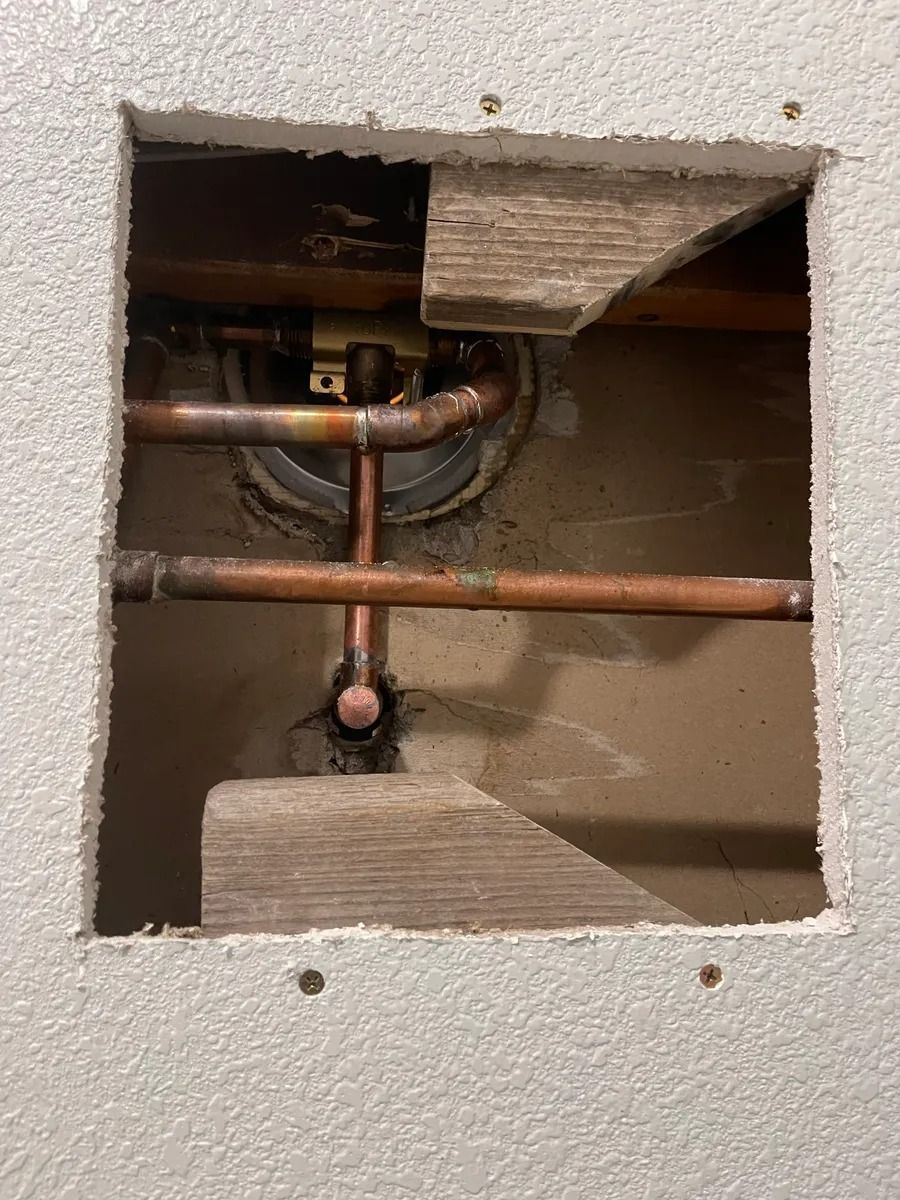 Open wall access panel showing exposed copper plumbing pipes and fittings.