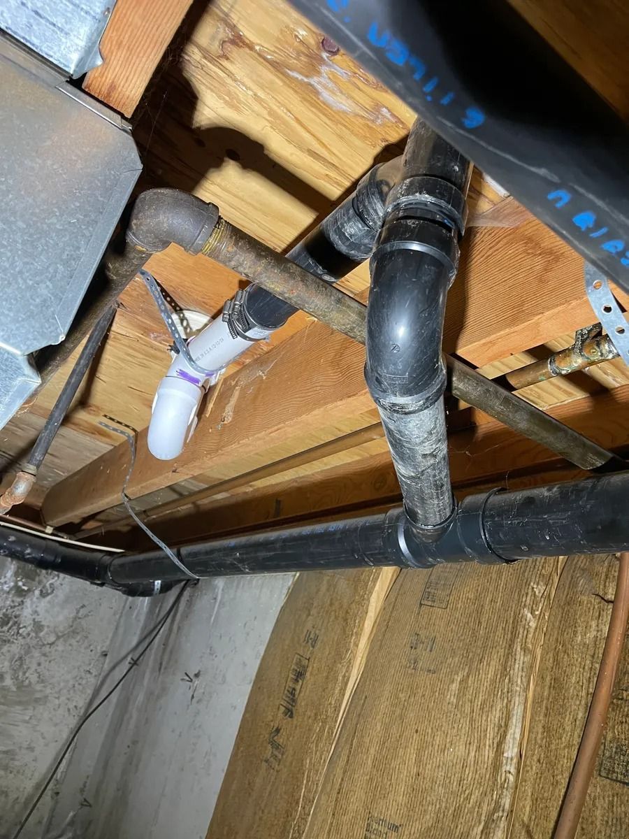 Damaged ceiling with exposed plumbing pipes, missing drywall, and a white PVC drain under wood framing