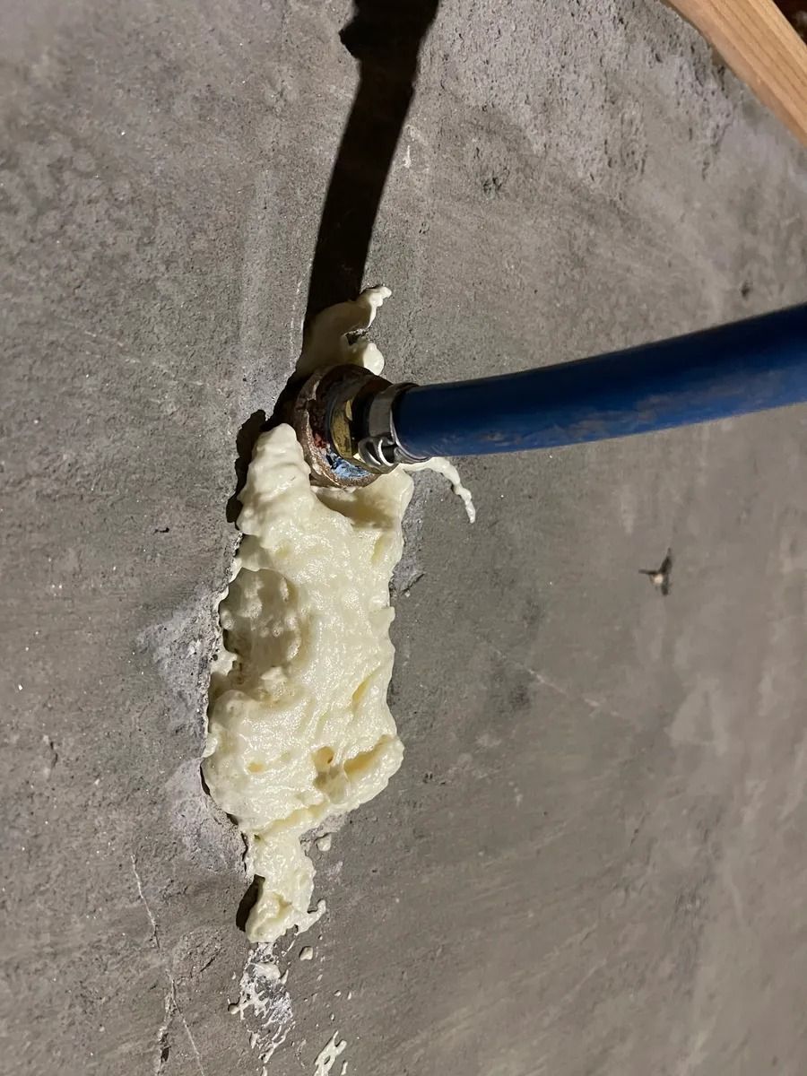 Blue cable entering a hole in a concrete wall with expanding foam sealing the gap