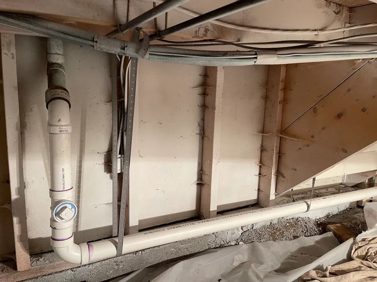 Exposed basement utility pipes and wiring along a rough unfinished wall and floor.