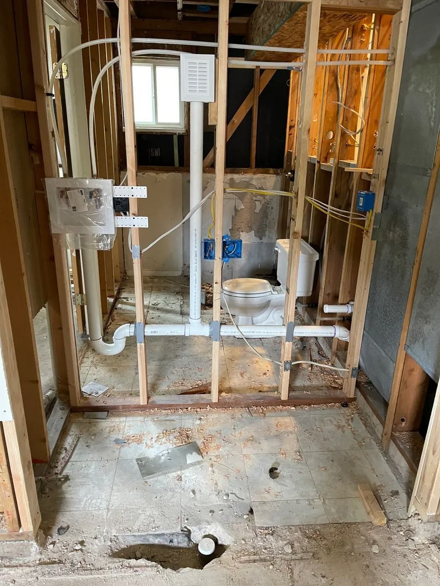 Unfinished bathroom with exposed studs, white plumbing pipes, and a toilet on a bare concrete floor