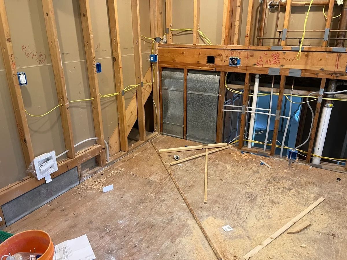 Unfinished room under construction with exposed framing, pipes, and debris on the floor