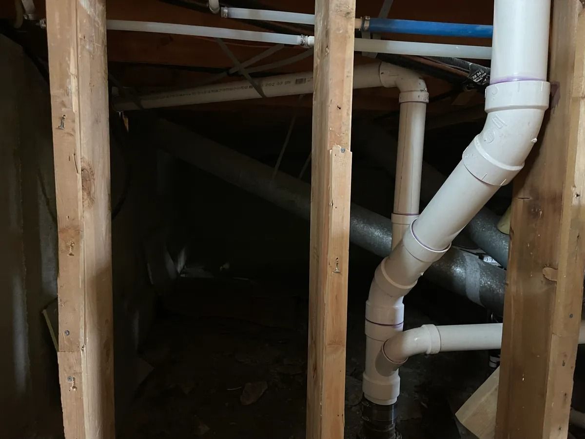Dark crawl space with exposed wooden beams and white pipes running through the framing