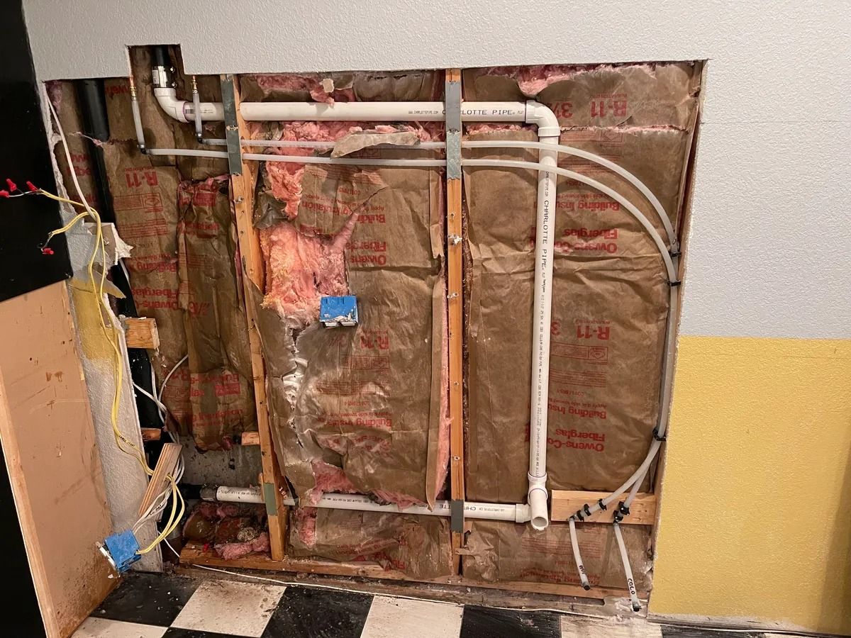 Exposed wall framing with insulation, wiring, and pipes in a partially demolished interior wall