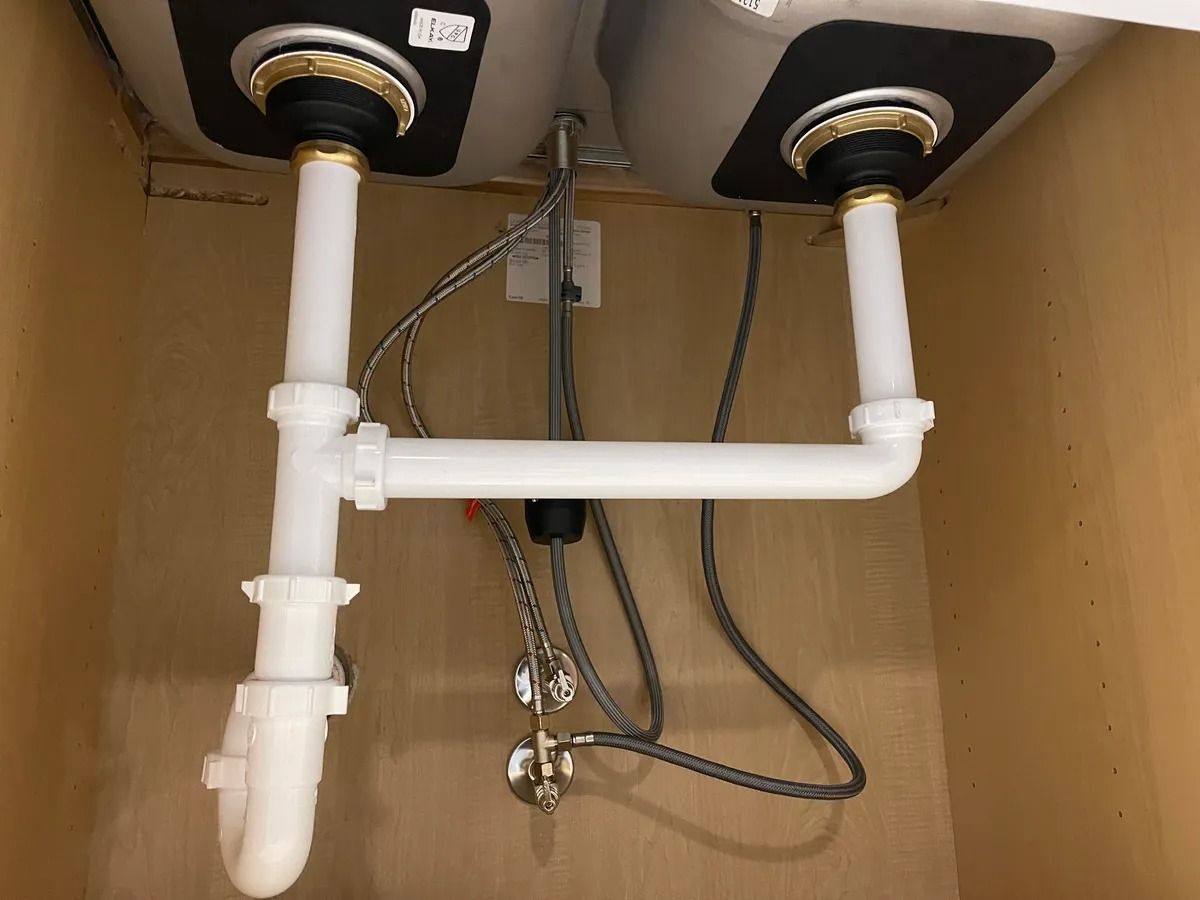Under-sink plumbing with white PVC pipes, drain traps, and exposed hoses in a cabinet
