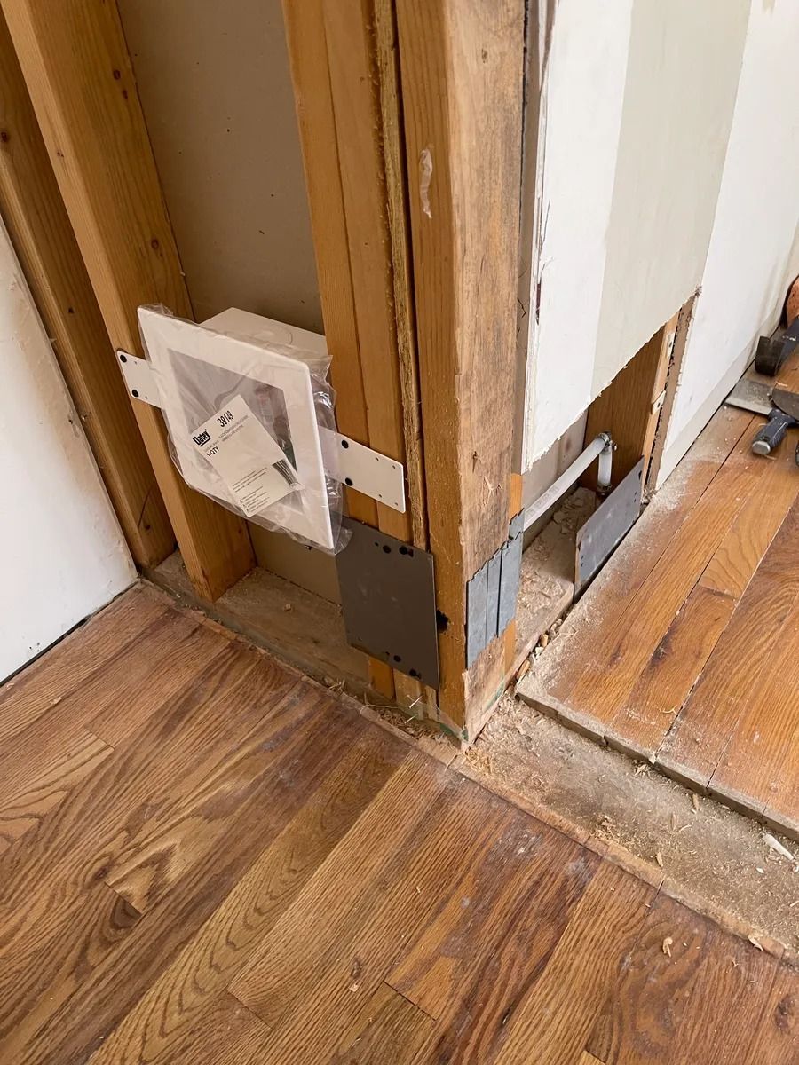 Electrical outlet and wall corner with exposed drywall and wood trim beside a hardwood floor.