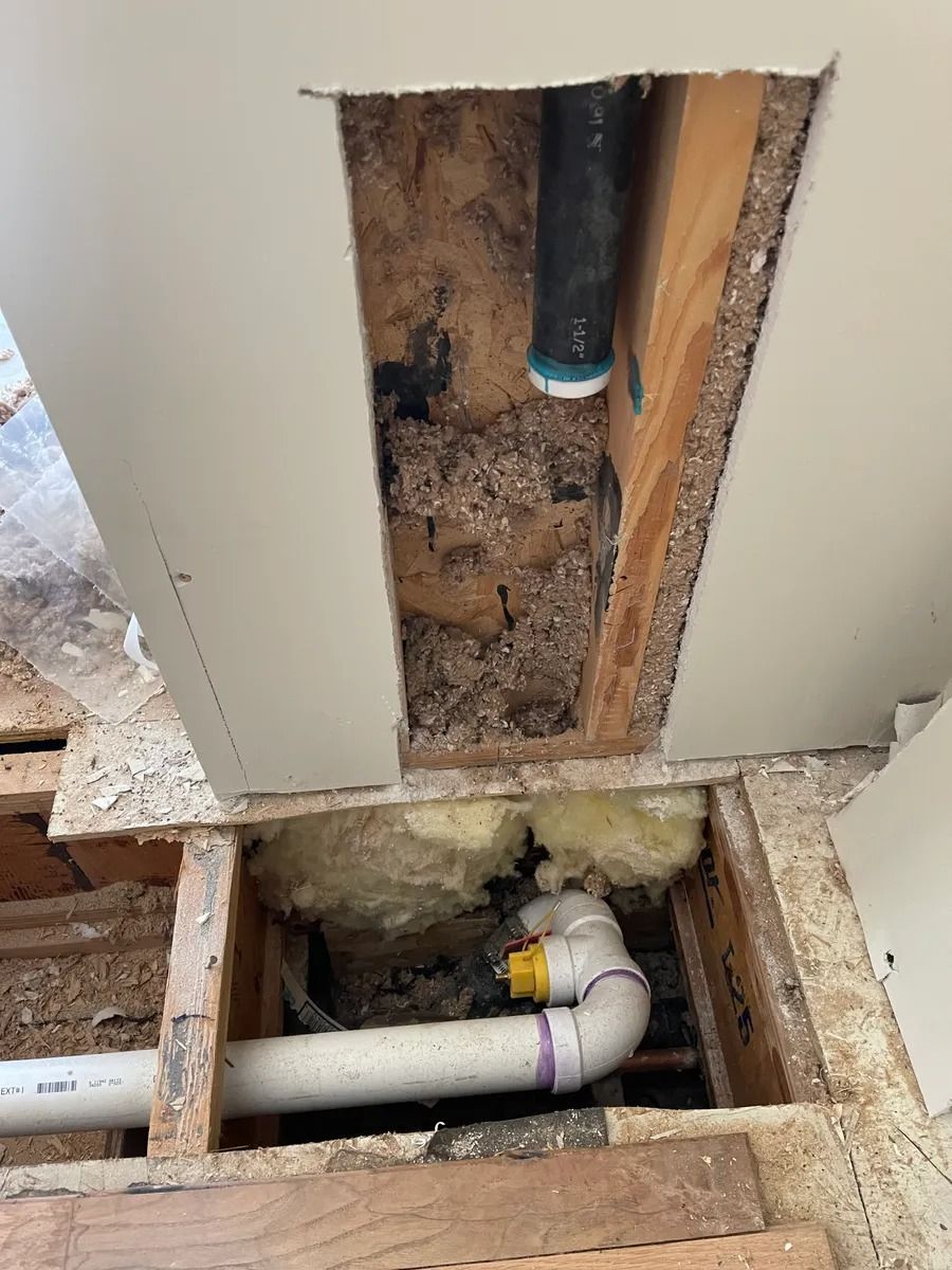 Open wall and floor cavity exposing plumbing pipes and insulation during construction